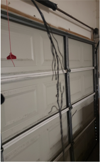 Close-up of a garage door with hanging cables in need of repair by Brentwood Garage Door Services.