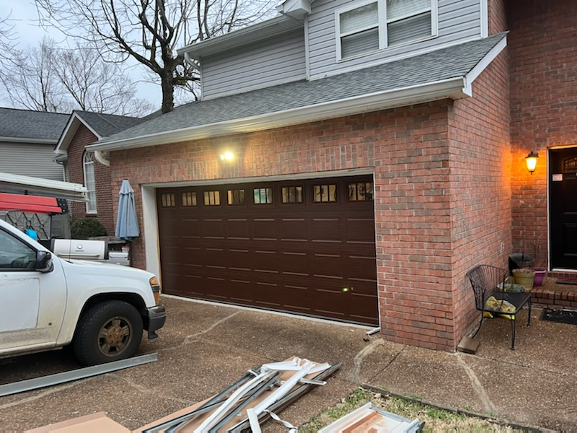 Brown garage door on a brick home with repair tools, by Brentwood Garage Door Services.